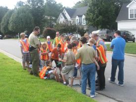 A group of people, some wearing orange safety vests, are huddled together on the street. 