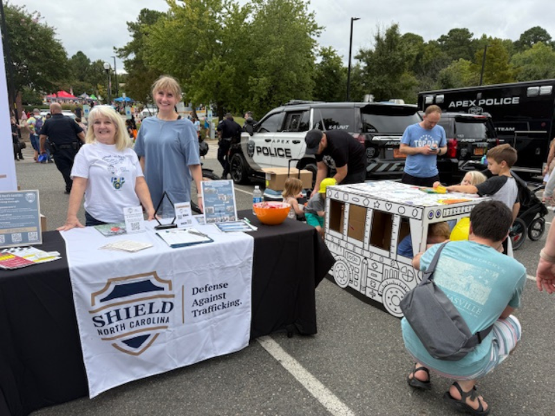 Image shows two people standing behind a table at an outdoor event